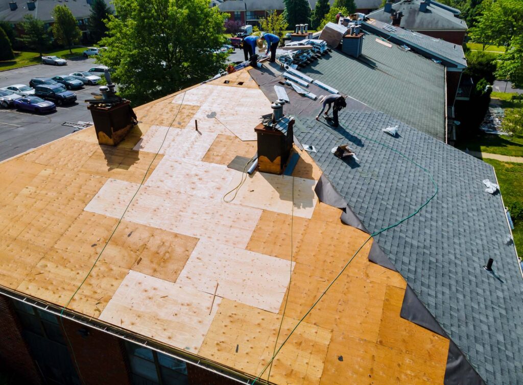 Roof replacement in progress on apartment building with new plywood decking and asphalt shingle installation
