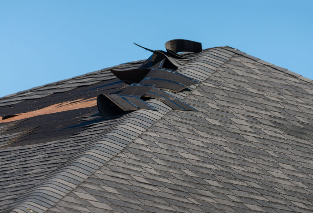 Storm-damaged asphalt shingle roof with missing roofing materials and exposed underlayment
