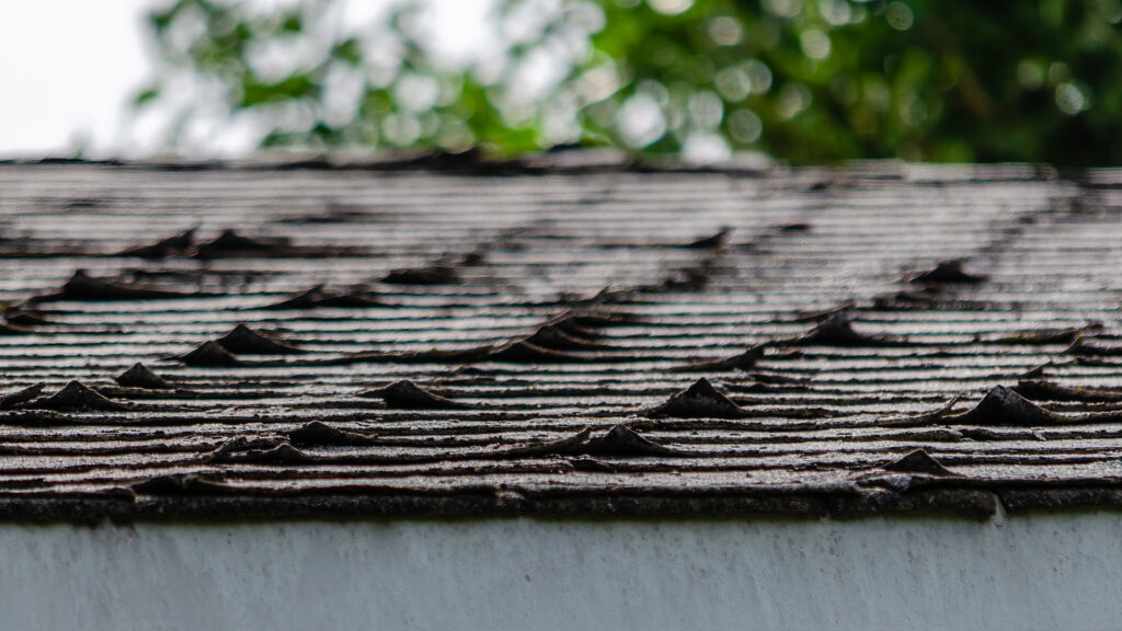 Close-up of worn and curling asphalt shingles showing signs of roof aging and deterioration